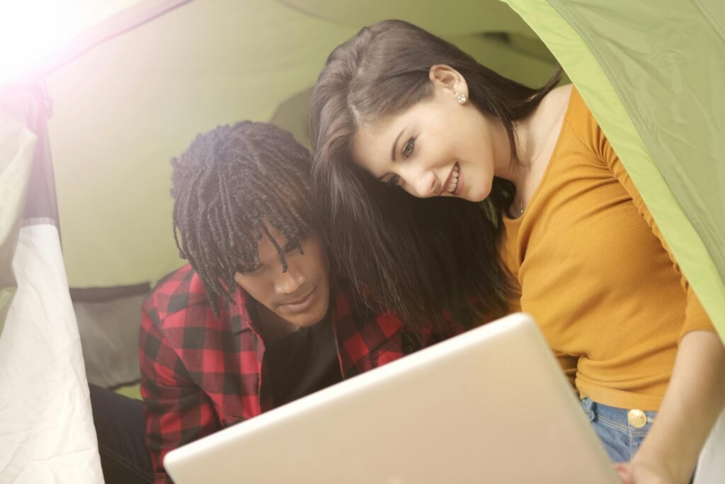 A young couple enjoying a laptop while camping in a tent during a sunny day.
