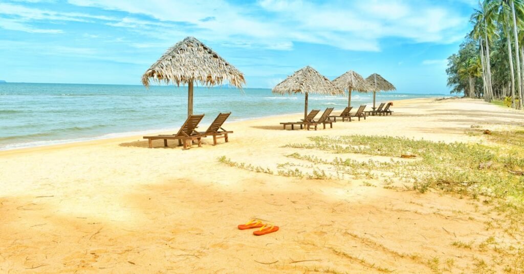 Idyllic tropical beach scene with empty lounge chairs under straw umbrellas on a sunny day.